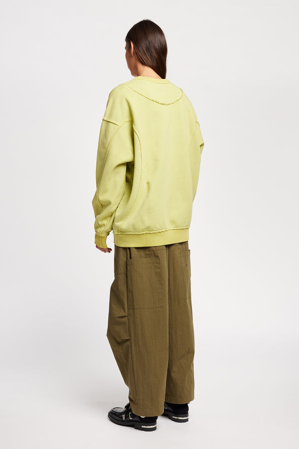 women - back of model wearing Unisex format oversized crew neck sweater in chartreuse with clean panelled design and raw flat-locked seams, displayed from the front.