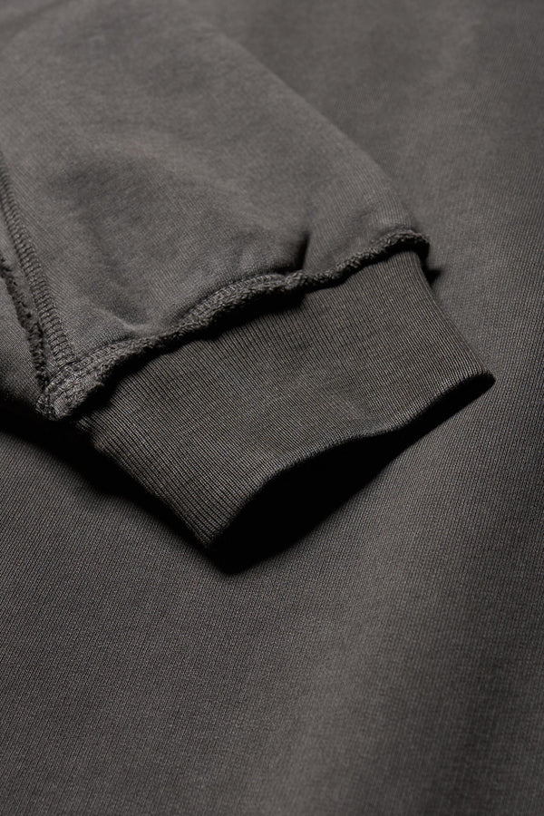 close up fabric details of Unisex format oversized crew neck sweater in jet black with clean panelled design and raw flat-locked seams, displayed from the front.