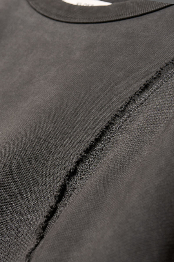 close up fabric details of Unisex format oversized crew neck sweater in jet black with clean panelled design and raw flat-locked seams, displayed from the front.
