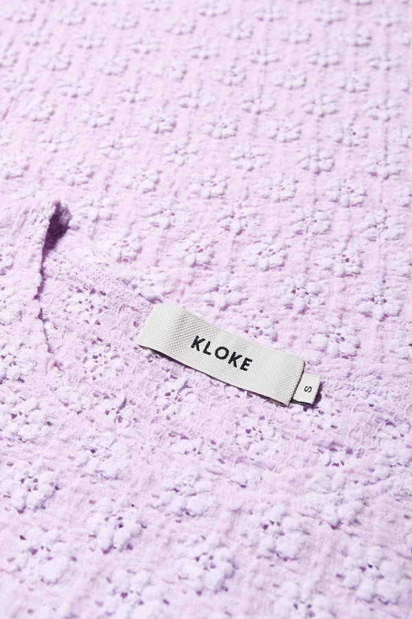 Close up fabric shot of the Ruse Top in Lilac, slim fit with cap sleeves and a flower motif, made from soft cotton with added stretch for comfort. Available in 6 sizes.