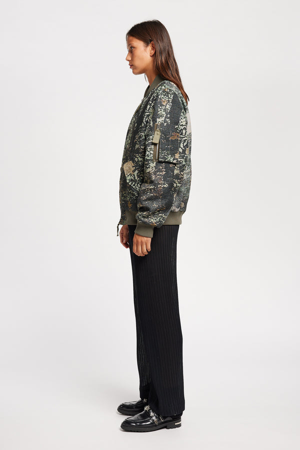 Women side of Unisex bomber jacket in Green Print woven jacquard with real tree camouflage, featuring dropped shoulders, ribbed trims, and full-length front zip.