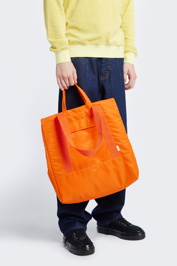 Model holding the Influx Padded Bag Orange, a practical tote with four compartments, including two snap-closing pockets. 