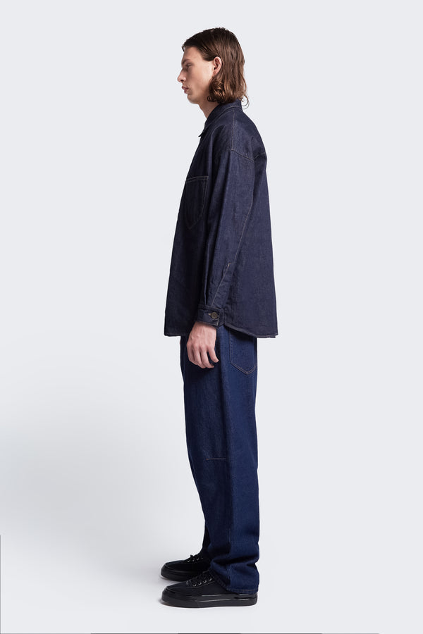 Side profile of the Barium Denim Shirt Indigo cut from Japanese denim with rounded hemline and long sleeves styled with the Grail Jeans Indigo.