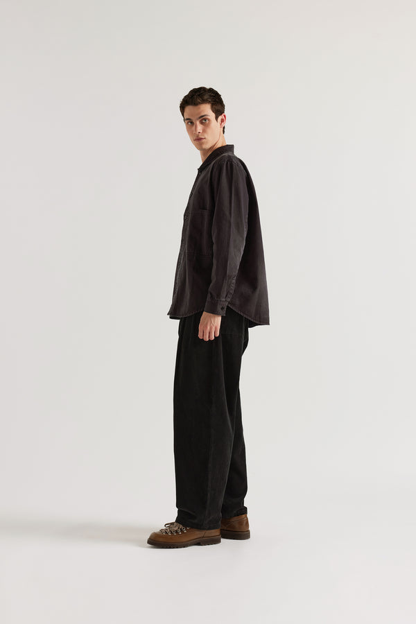 Side view of the black Dissolve Cord Pant showing double-pleated front, loose fit and deep rich corduroy colour from garment double over-dye process