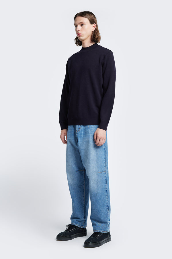 Model wears the Dose Merino Sweater Ink, knitted in a fine Merino wool in a milano knit construction, this mock-neck style is finished with a 1x1 rib hemline and cuffs. This sweater is a cool weather staple and is styled with the Grail Jeans Mid Blue Fade.