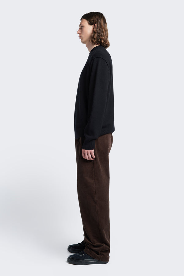 Side profile of the Intake Pleat Pant Chocolate, a semi-tailored cord pant with a loose, double-pleated fit. Featuring side slant-pockets and two button-closing back pockets.