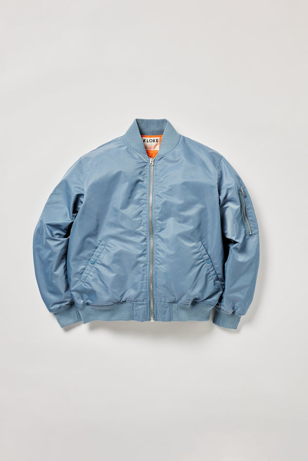 Flat front of the Grey Blue Lyric Bomber Jacket in garment-washed nylon with zip front, tonal ribbing and multiple utility pockets.