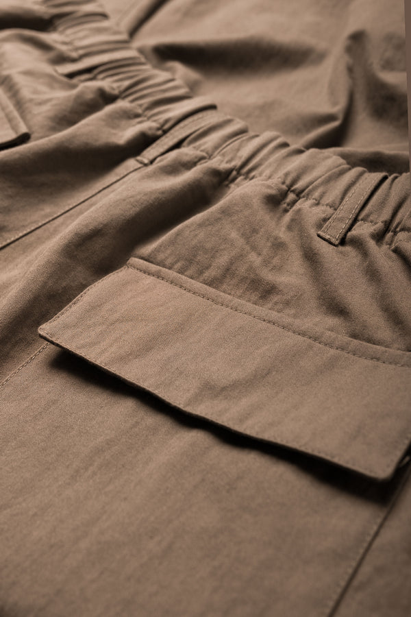 The Modulate Cargo Pant Mid Brown features an elastic waist with classic zip and press-stud fly closure and six pockets including flap pockets at the back. 