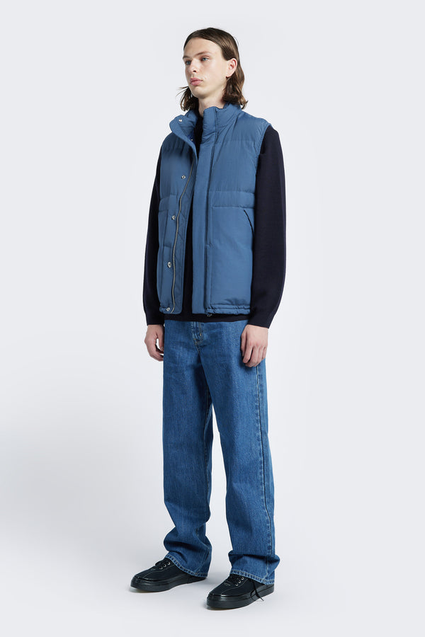 The Reset Quilted Puffer Vest Blue features a high neckline, centre front zip and stud press closure, internal and side pockets and adjustable toggled elastic waist. Made with 100% post-consumer down fill.