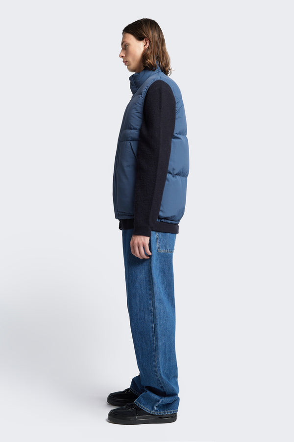 Side profile of the Reset Quilted Puffer Vest Blue with elasticated arm holes for comfort and an adjustable toggled elastic waist. Styled with a sweater and Jeans.