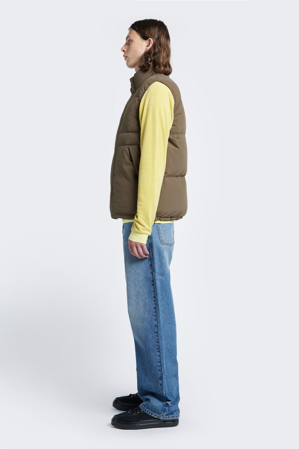 Side profile of the Reset Quilted Puffer Vest Brown with elasticated arm holes for comfort and an adjustable toggled elastic waist. Styled with a sweater and Jeans.