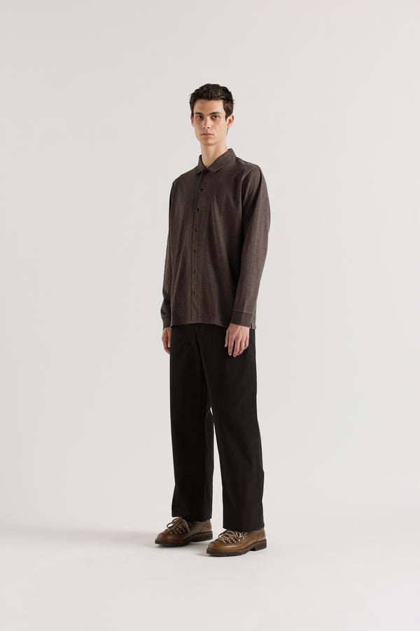 Front angle of the male model in black licorice Shadow Jersey Shirt in a pigment-dyed slub cotton with a relaxed boxy fit and button-through front.