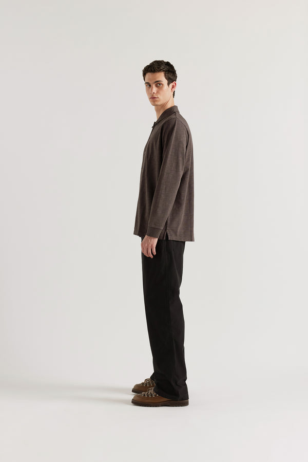 Side profile of the male model in black licorice Shadow Jersey Shirt in a pigment-dyed slub cotton with a relaxed boxy fit and button-through front.