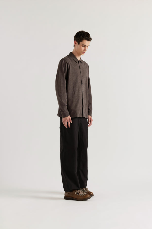 Front angle of the male model in black licorice Shadow Jersey Shirt in a pigment-dyed slub cotton with a relaxed boxy fit and button-through front.e