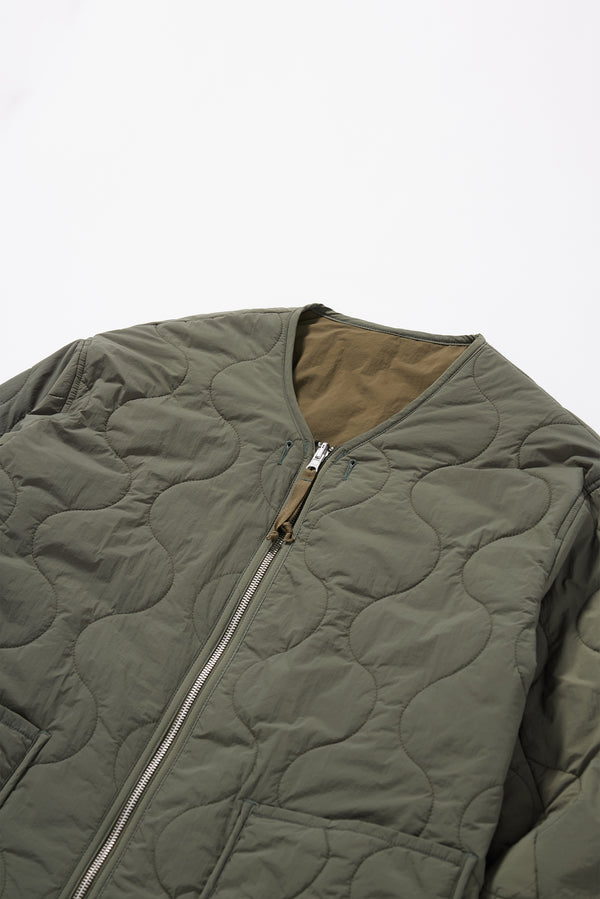 Close-up detail shot of ripple-patterned quilted stitching on olive recycled nylon reversible jacket. Showcasing Pocket, zip and cuff detailing. 