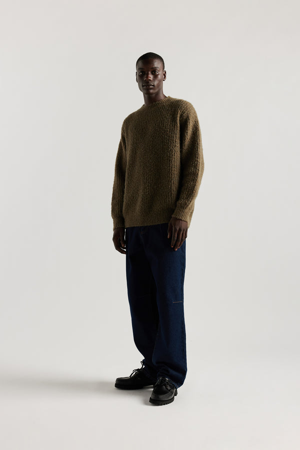 Model in Olive Spore Knit Sweater front view showing crew neck raglan silhouette, fluffy marle-flecked alpaca blend knit and exposed seam linking detail