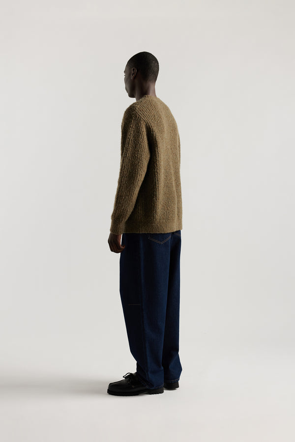 Back view of model in the Olive Spore Knit Sweater showing raglan sleeve construction, exposed seam linking and fluffy alpaca blend reverse cardigan knit