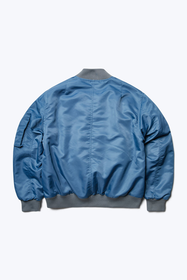 The back of the Bomber Jacket Blue, a lightweight nylon jacket with rib trim. This jacket is a homage to the original MA-1. 