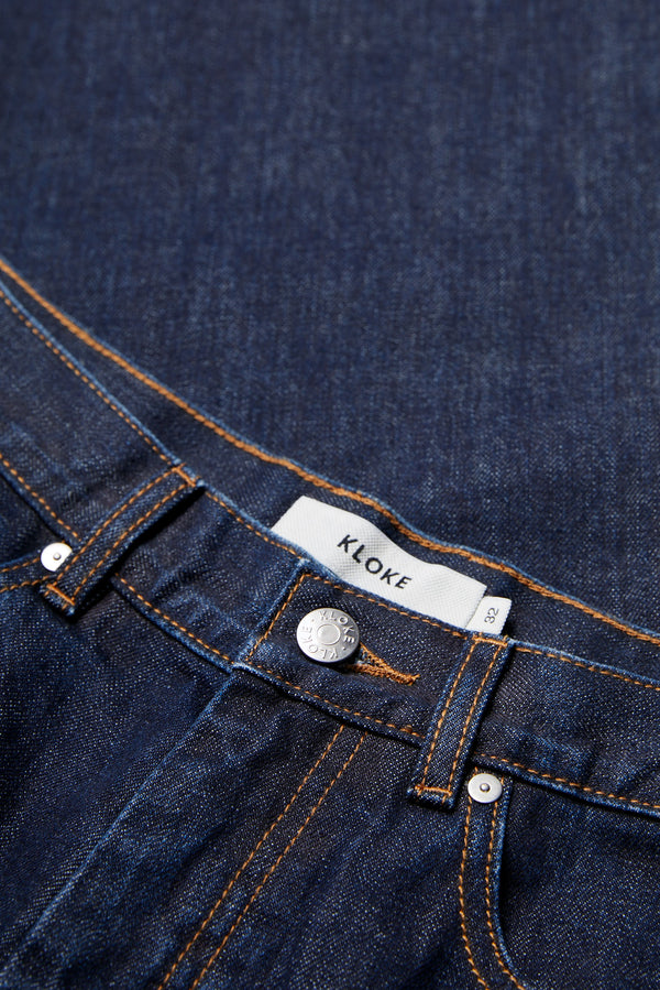 Close up details of the sworn denim jean in Indigo. Looser fit all-purpose jeans in premium Japanese denim with zip fly, button closure, five-pocket design, and Kloke branded hardware. Available in 8 sizes.