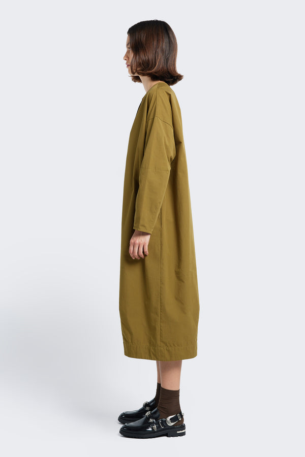 Model standing side on wearing the Agora Dress Moss Green with long sleeves and in seam side pockets.