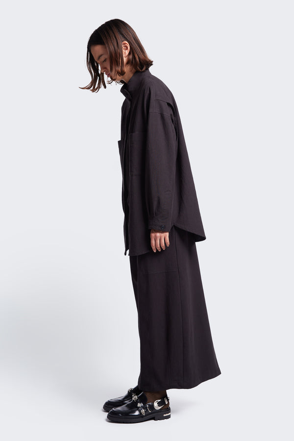 Side profile of the Anima Skirt Black, a long, straight style skirt with elasticated waistline, back centre split, darted panels and straight hem. 