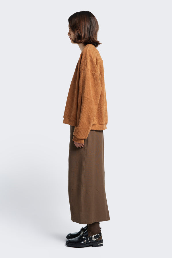 Side profile of the Anima Skirt Brown, a long, straight style skirt with an elasticated waist and back centre split. 