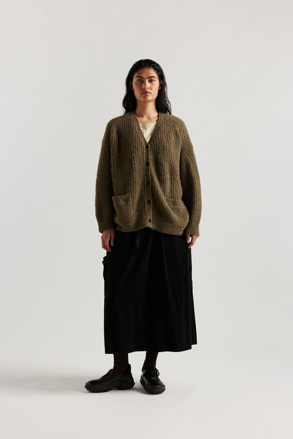 Female model in Olive Bloom Cardigan worn open and layered over a Tee and Skirt, showing relaxed oversized silhouette and fluffy alpaca blend texture
