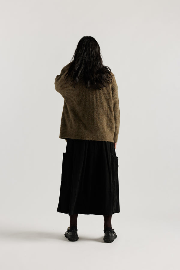 Back of female model in Olive Bloom Cardigan worn open and layered over a Tee and Skirt, showing relaxed oversized silhouette and fluffy alpaca blend texture