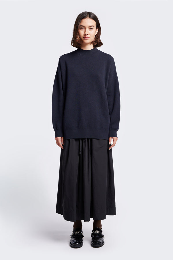 The Buro Knit Sweater in Ink is a mock neck merino sweater crafted in a milano knit structure. Model wears sweater styled with the Interlude Skirt Black.