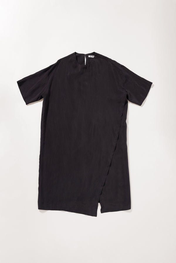 Flat front of the Eon Dress in vintage black  showing fluid midi silhouette and double-layered asymmetric split front.