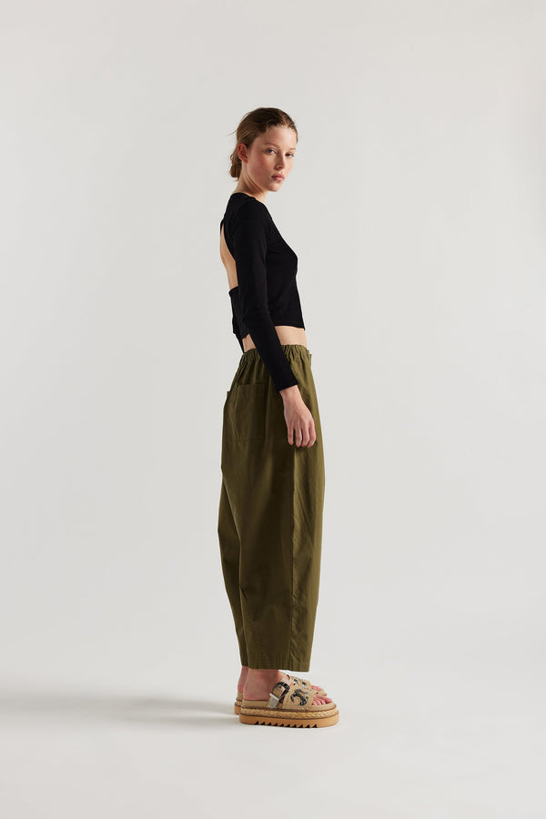 Side view of the model in the Factor Pleat Pant Olive Green.  A relaxed silhouette defined by an encased elastic waistband. 