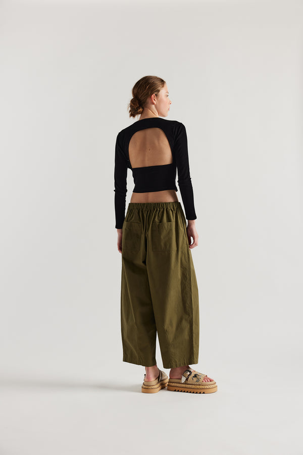 Back view of the model in the Factor Pleat Pant Olive Green.  A relaxed silhouette defined by an encased elastic waistband