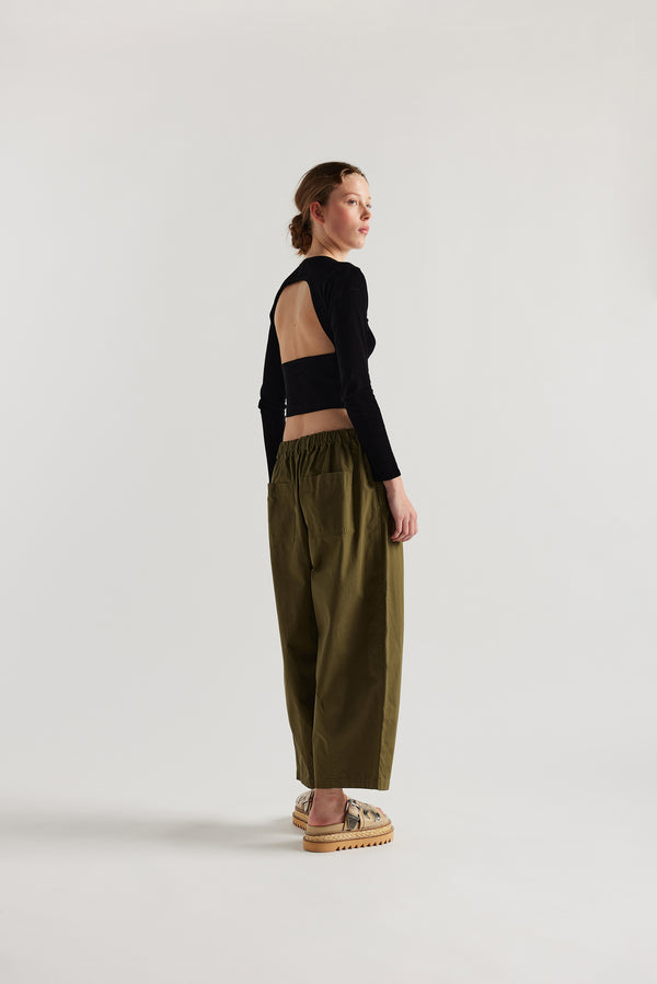 Back view of the model in the Factor Pleat Pant Olive Green.  A relaxed silhouette defined by an encased elastic waistband. 