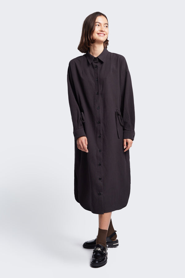 The Filter Dress Black, a classic and comfortable style with a button through partly concealed placket and built in collar, in seam side pockets and rounded scoop hemline. 