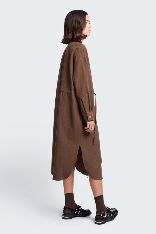 Side profile of the Filter Dress with side split, long sleeves and rounded hemline. Made from 100% cotton in Brown. 