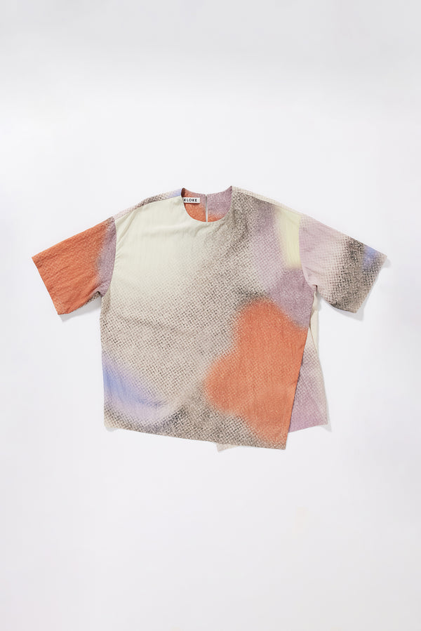 Flat front of the Glimmer Top in Aion Print front view showing round neck, short sleeves, asymmetric split front and fragmented mauve, blue and orange deity print