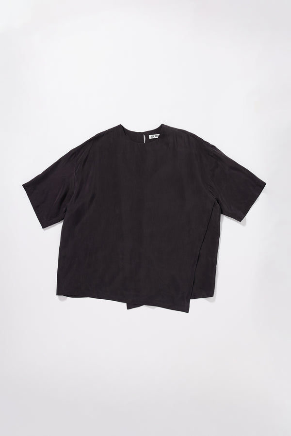Flat front of the Glimmer Top in washed vintage black cupro featuring a double-layer asymmetrical front and fluid silhouette.