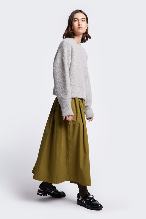 The Hold Shearling Sweater Soft Grey, a special shearling knit made from an Alpaca blend that's soft. This sweater has a flattering silhouette with cropped hem and dropped shoulder. The model wears the sweater with the Interlude Skirt Moss Green.