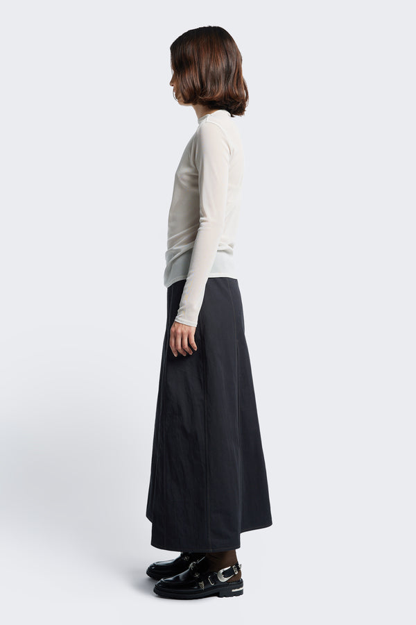 Side profile of the Idle Skirt Black, a godet style skirt with contrast stitch details, in seam side pockets and centre back zip closure. 