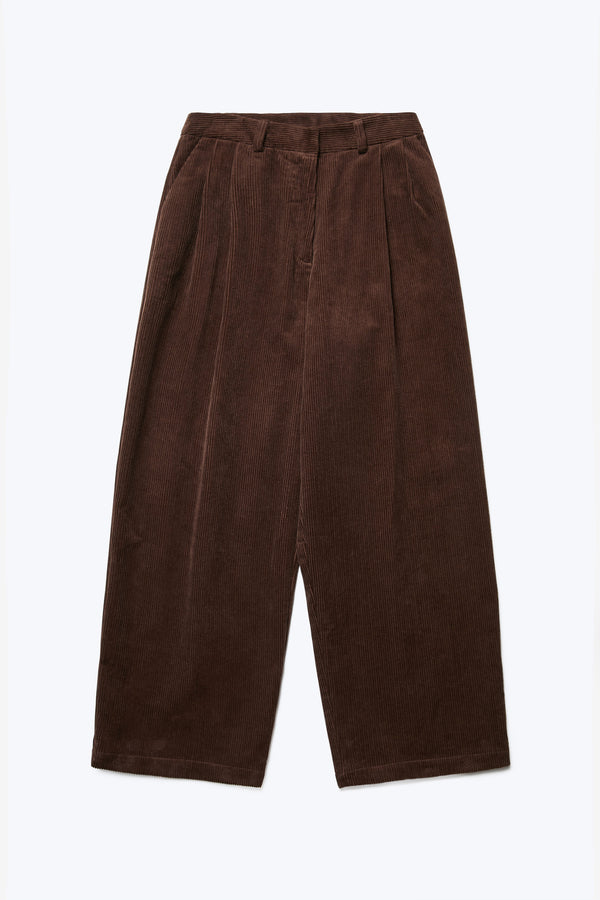 The front of the Interim Pant Dark Brown, a semi-tailored cord pant with a generous and flattering double-pleated fit. Featuring side slant-pockets and two button-closing back pockets to keep valuables safe. 