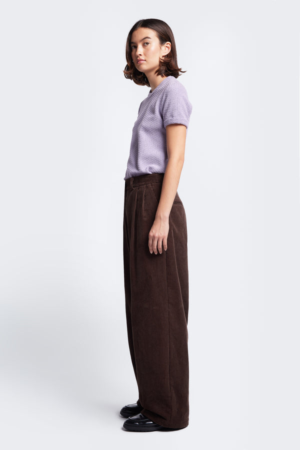 Side profile of the Interim Cord Pant Dark Brown, a semi-tailored pant with a generous and flattering double-pleated fit.