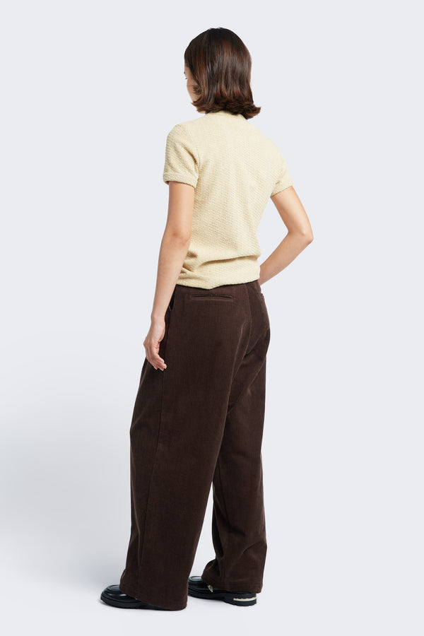 The Interim Pant Dark Brown, a semi-tailored cord pant with a generous and flattering fit. Featuring two button-closing back pockets to keep valuables safe. 