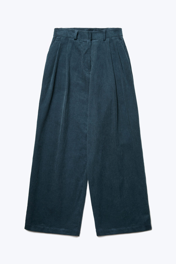 The front of the Interim Pant Petrol Blue, a semi-tailored cord pant with a generous and flattering double-pleated fit. Featuring side slant-pockets and two button-closing back pockets to keep valuables safe. 