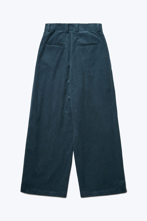 The back of the Interim Pant, a semi-tailored cord pant in Petrol Blue with a loose fit. Featuring two button-closing back pockets to keep valuables safe.