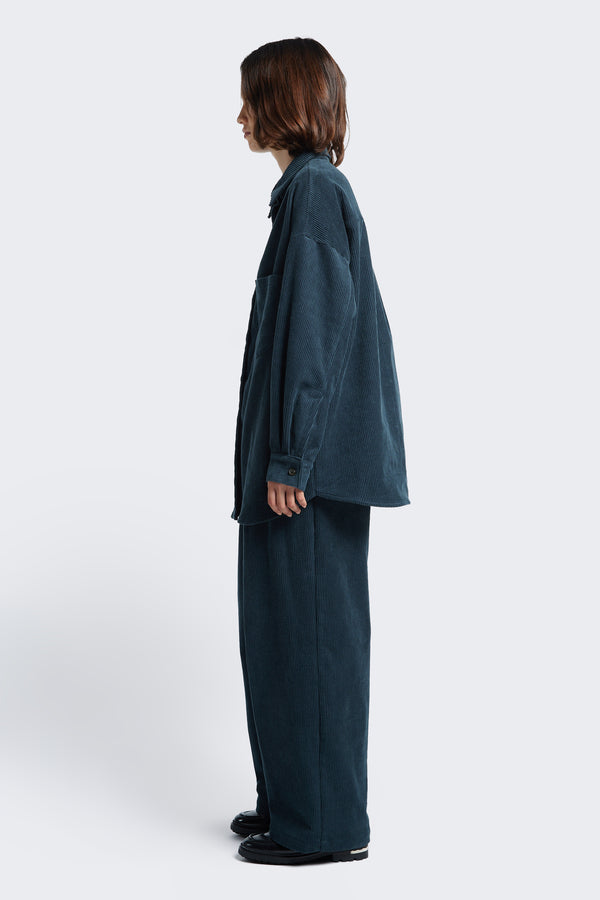 Side profile of the Interim Cord Pant Petrol Blue, a semi-tailored pant with a generous and flattering double-pleated fit.