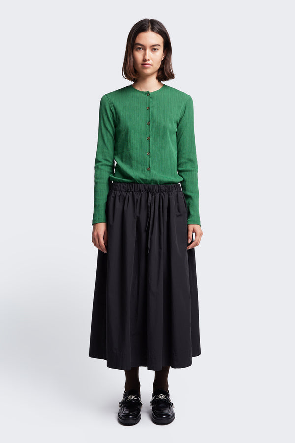 The Interlude Skirt Black, a mid-length, full, gathered skirt with an elasticated waistband. Features two front welt pockets. Available in five sizes.