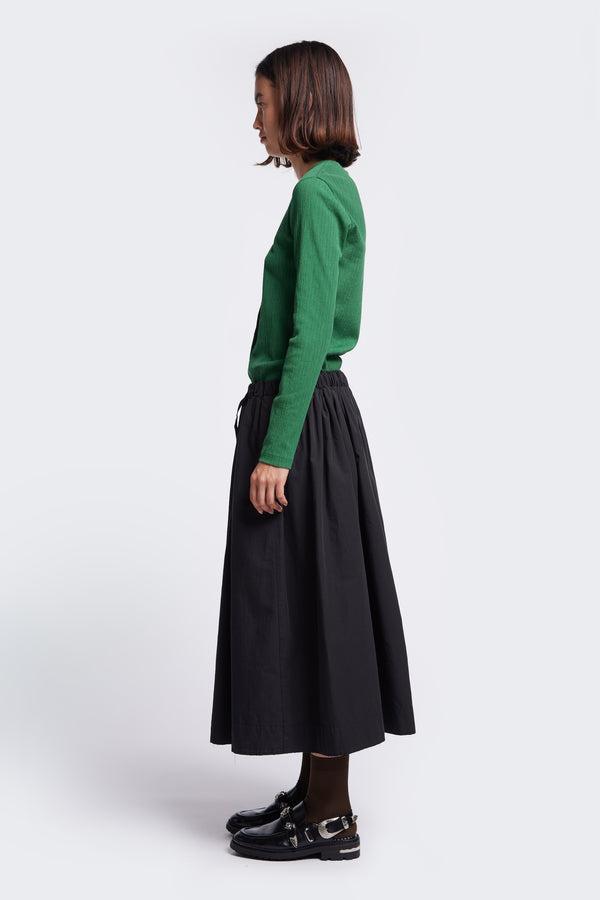 Side profile of the Interlude Skirt Black  a full gathered skirt with an elasticated waistband and  two front welt pockets. Made from 100% cotton. 