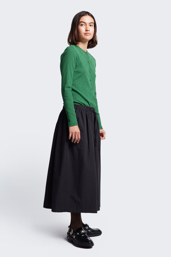 The Interlude Skirt Black has a full, gathered skirt, elasticated waist, and raw hem. Styled with the Hideout Crinkle Top Green.