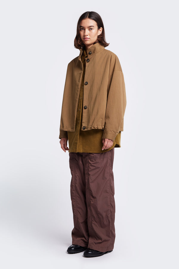 Models wears the Embark Jacket Tan, a wide crop blouson style jacket with centre front button closure. This jacket is a relaxed style with drop shoulders going into a cuff sleeve opening.