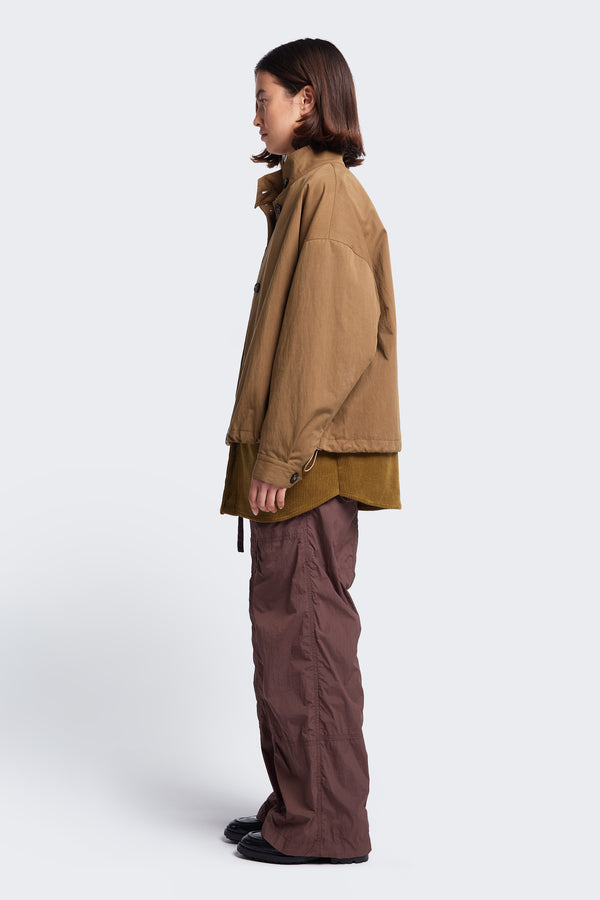 Model stands side on wearing the Embark Jacket Tan a relaxed wide crop blouson style jacket with drop shoulders going into a cuff sleeve opening. The dropped shoulders accentuate a boxy silhouette.